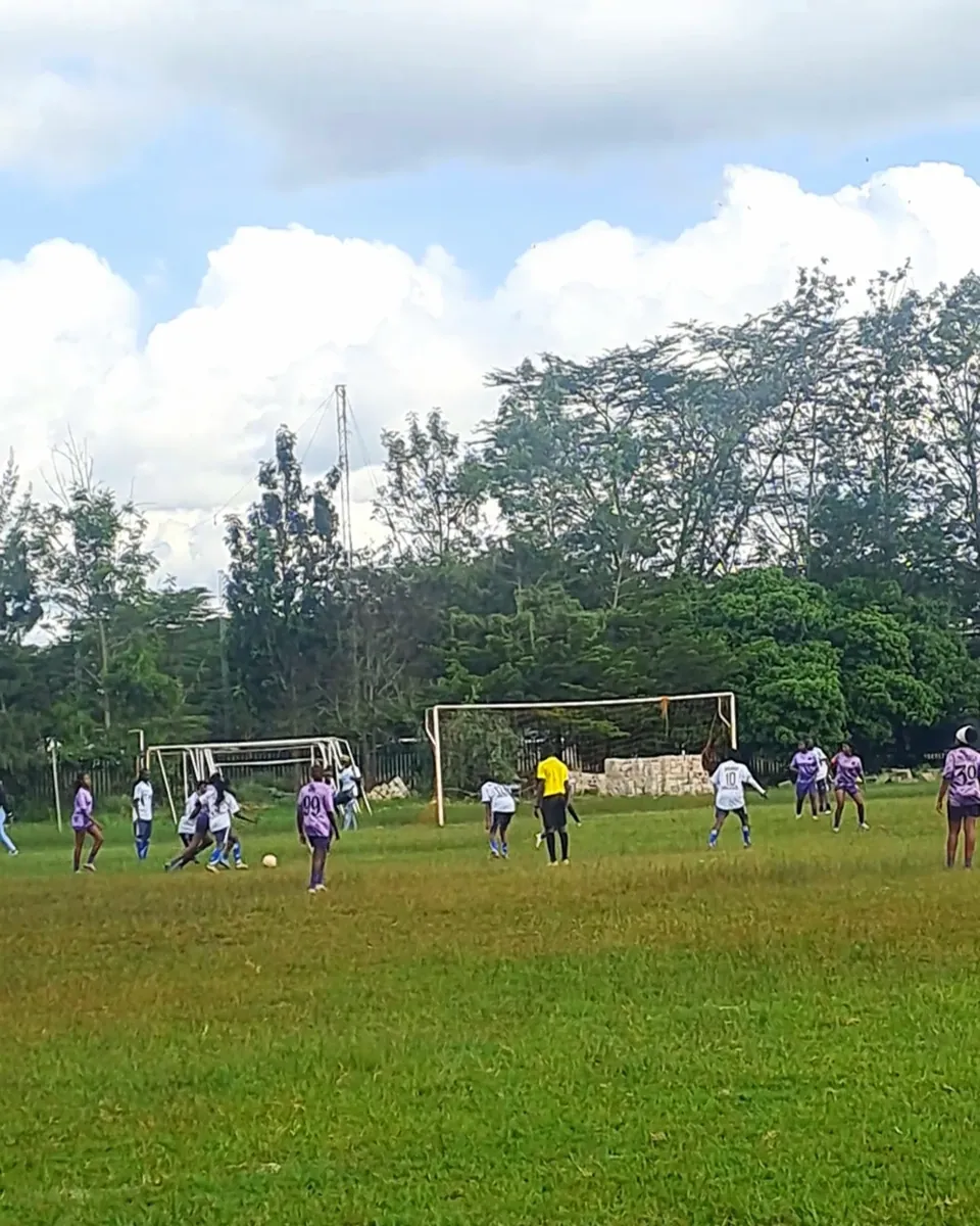 An open field with a goal and players warming up under a wide sky
